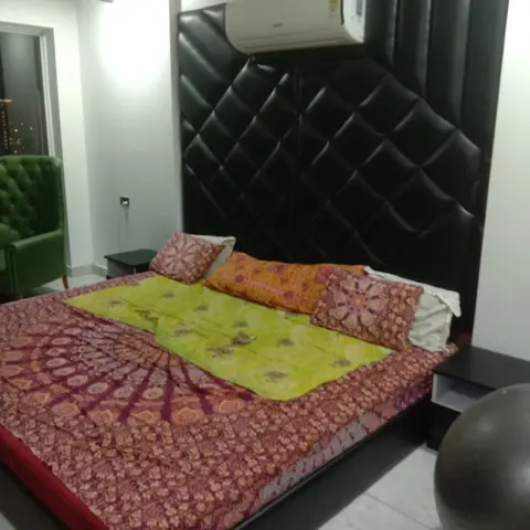 King bed with a tall black diamond-tufted leather headboard wall, styled with a mismatched patterned bedsheet