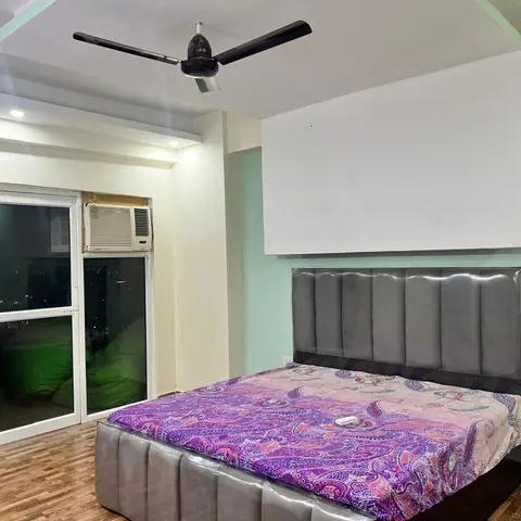 King-size bed with a grey tufted headboard against a mint-green accent wall and an unfinished-looking white patch above it, wood-look flooring