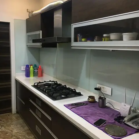 Kitchen counter with dark wenge-finish shutters, a frosted glass backsplash, and a glass-front upper cabinet, counter cluttered with a wifi router