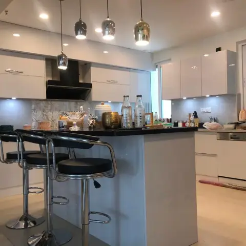 Kitchen island with a cluster of graduated glass pendant lights, glossy white cabinetry, a black granite counter, and chrome-legged bar stools.