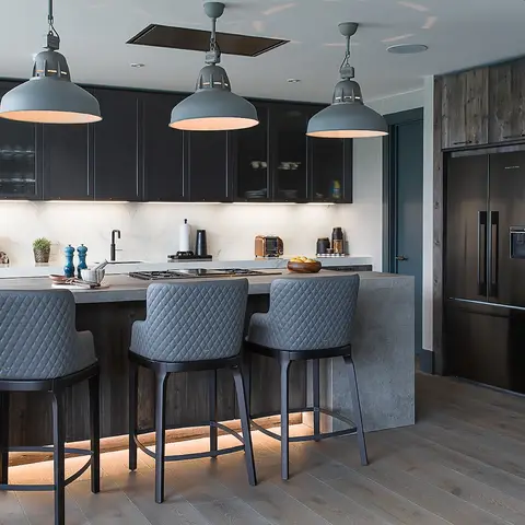 Kitchen island with a concrete-look waterfall countertop, three grey industrial dome pendant lights, and quilted grey barstools