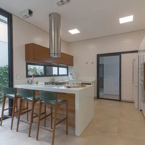 Kitchen island with a white waterfall countertop, a cylindrical stainless steel chimney hood, and white brick-tile walls