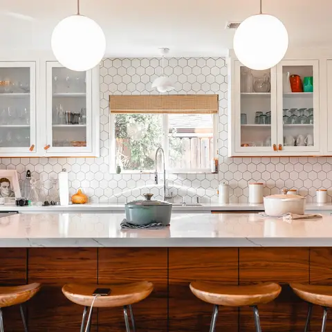 Kitchen island with a white waterfall-edge counter, walnut-front cabinetry, hexagon tile backsplash and four wood swivel bar stools.