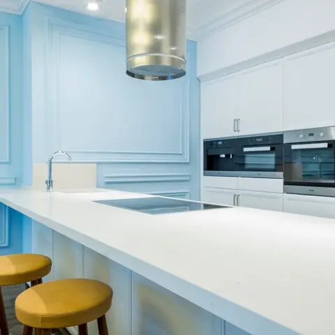 Kitchen island with white waterfall quartz countertop and a cylindrical steel pendant hood, flanked by pale blue panel-moulded walls