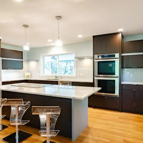 Kitchen with a dark wood island topped in white marble, clear acrylic bar stools, twin pendant lights