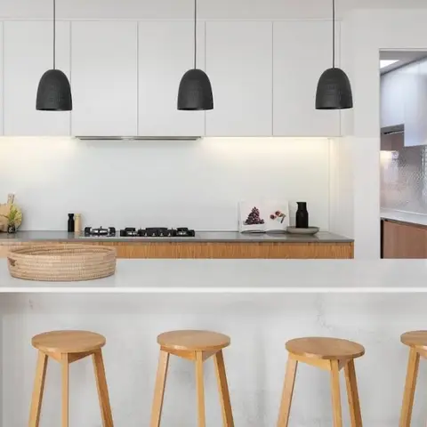 Kitchen with a white waterfall-edge island seating four oak stools, three black dome pendants above, oak-veneer cabinetry