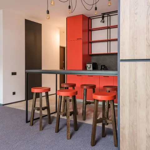 Kitchen with bold red-orange gloss cabinetry and matching open shelving, a black metal breakfast bar with red stools, and exposed-bulb pendant lights