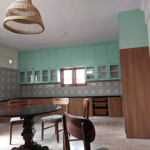 Kitchen with mint-green upper shutters, a patterned tile backsplash, and a round wood dining table with a woven rattan pendant light.