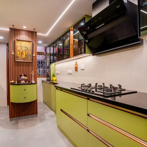 Kitchen with olive green glossy shutters and rose-gold trim, black granite counters, and a curved built-in pooja niche framed by fluted wood panelling.