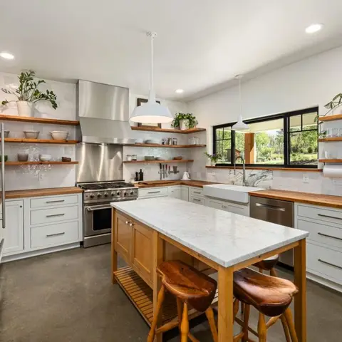 Kitchen with white shaker cabinetry, butcher-block wood countertops and open wood shelving styled with glassware and plants