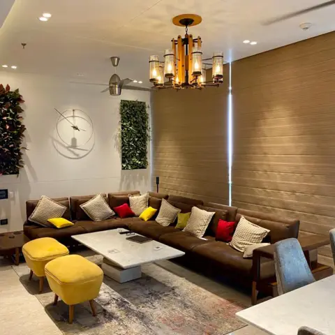 L-shaped brown leather sectional with yellow velvet ottomans around a marble coffee table beneath a bamboo-style pendant chandelier