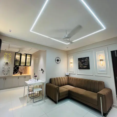 L-shaped channel-tufted brown velvet sofa in a living room with a diamond-shaped LED ceiling light profile and moulded wall panels holding a metal Buddha wall