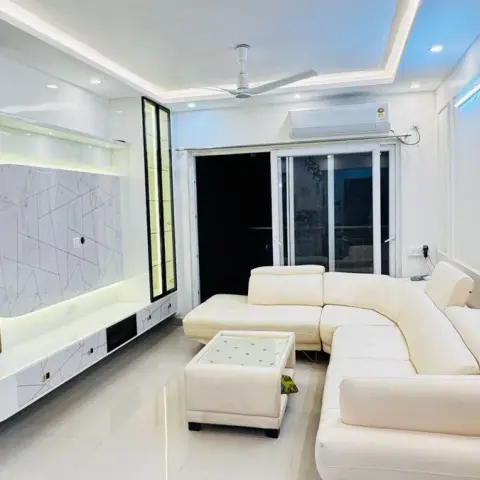 L-shaped cream sectional sofa facing a curved fluted-wood TV unit with a backlit oval marble-pattern panel, in a living room with cove ceiling lighting