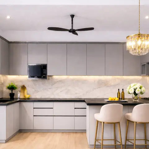 L-shaped grey modular kitchen with a marble-look backsplash and black countertop island seating three gold-legged bar stools under a crystal chandelier.