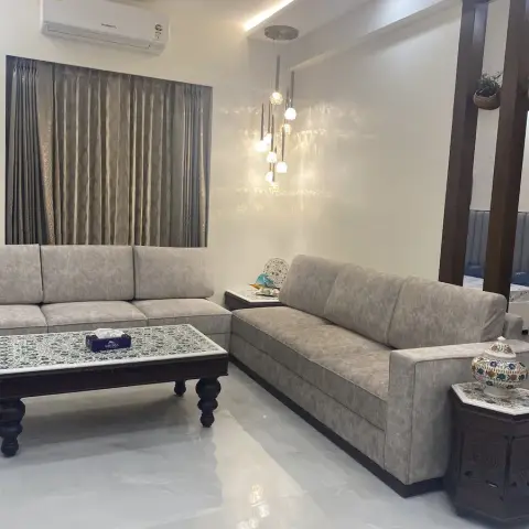 L-shaped grey sofa set around a carved wood coffee table with tile inlay, lit by a cascading cluster pendant and a cove-lit ceiling