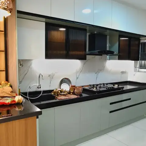 L-shaped kitchen in sage-green gloss with white overheads and reeded brown-glass cabinets flanking a black chimney