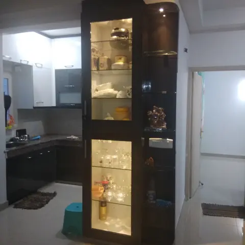 L-shaped kitchen with a dark curved glass-front crockery display cabinet acting as a room divider, backlit shelves showing glassware and kitchenware