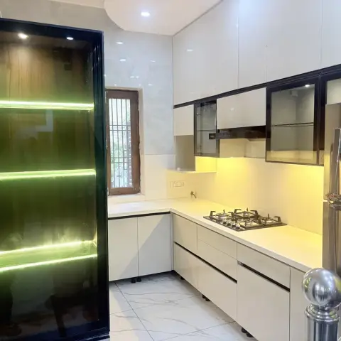 L-shaped kitchen with cream glossy cabinetry, black-framed glass wall units with warm under-lighting, a gas hob