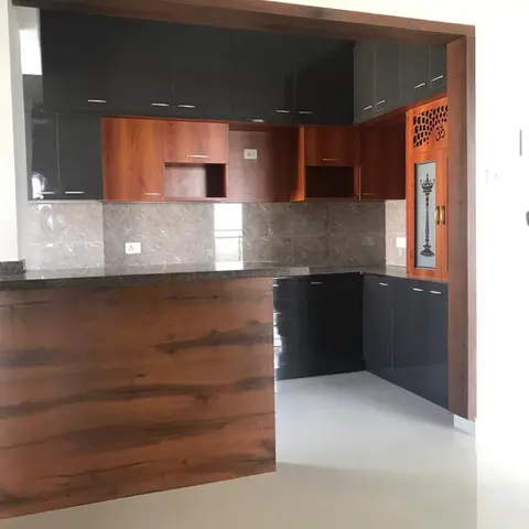 L-shaped kitchen with glossy black cabinetry, wood-grain accent doors and a built-in jaali pooja unit in the corner