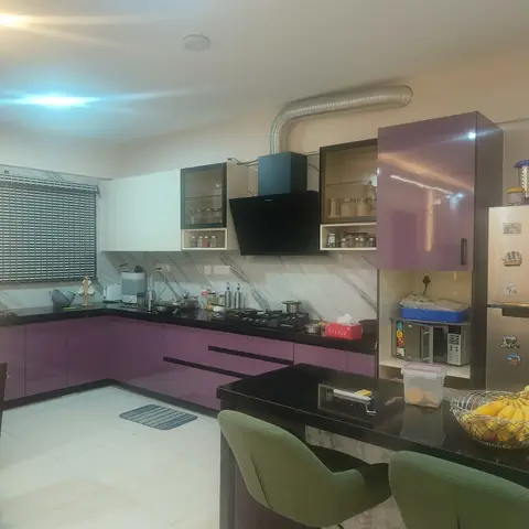 L-shaped kitchen with glossy purple cabinetry, black granite countertops, a marble-look backsplash and a black stone breakfast counter with green upholstered