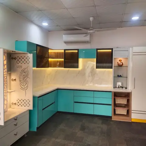 L-shaped kitchen with glossy turquoise modular cabinets, a marble backsplash, and an adjoining jaali-pattern pooja unit with a peacock motif