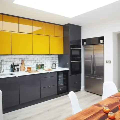 L-shaped kitchen with high-gloss yellow upper cabinets over charcoal lower units, white subway-tile splashback and an integrated stainless steel fridge-freezer