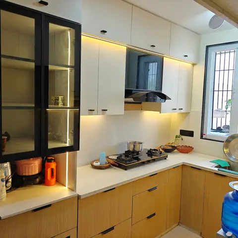L-shaped kitchen with wood-grain laminate lower cabinets, white upper units, a black-framed glass display cabinet with LED lighting