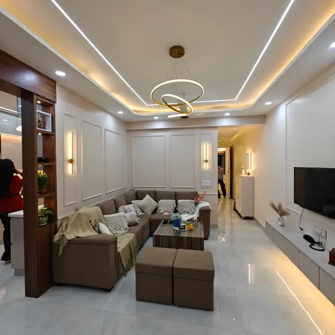 L-shaped living room with a box-profile cove-lit false ceiling, a gold ring pendant, panel-moulded accent wall