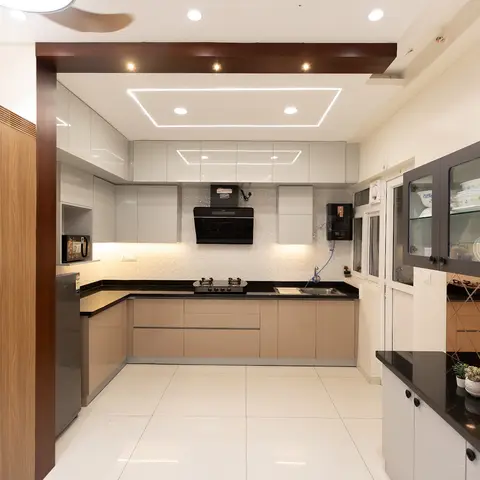 L-shaped modular kitchen with taupe glossy shutters and black granite counters, opening past a carved wood jaali partition hung with a toran