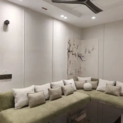 L-shaped sage-green sofa banked with bouclé cushions in a cream groove-panelled corner