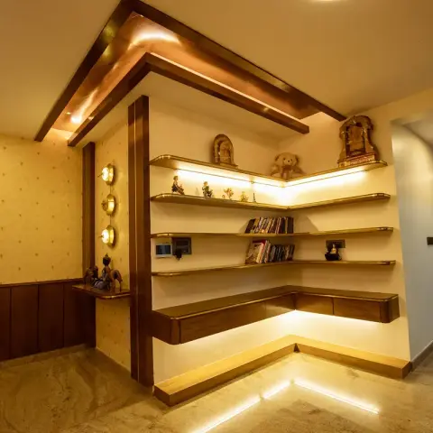 L-shaped wall-hung wooden study counter wrapped into a corner, its stepped floating shelves lit strip by strip and holding brass idols