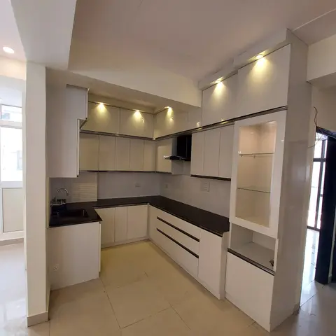L-shaped white gloss modular kitchen with black granite counters and a glass-shelved display unit at the open end.