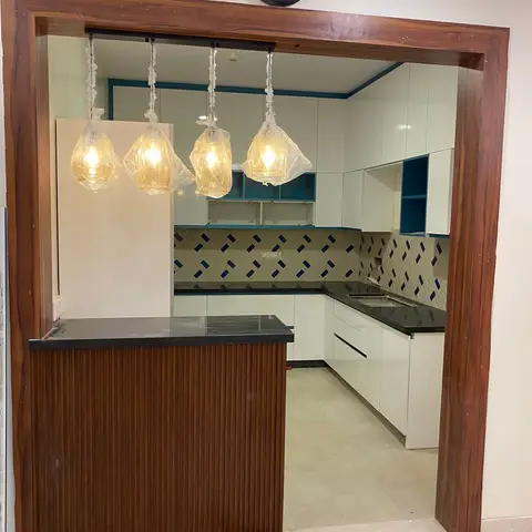 L-shaped white glossy kitchen seen through a timber portal frame past a fluted-wood breakfast counter