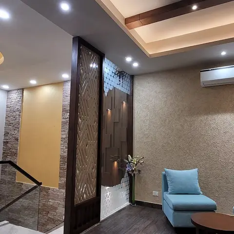 Landing lounge with a sand-textured accent wall, a carved wood jaali partition, and a pair of powder-blue armchairs around a round coffee table.