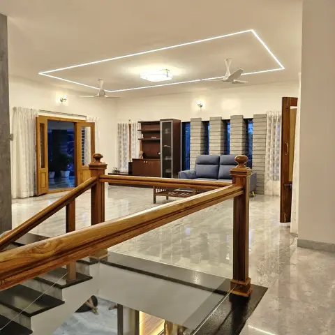 Landing over a wooden-railed staircase looking into an open living room with a grey sofa, a wood-and-glass crockery unit and stone-clad window bays.