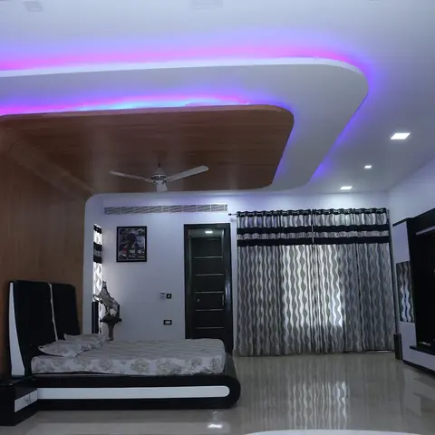 Large bedroom washed magenta by an RGB cove, where a curved wood-laminate panel sweeps out of the false ceiling and down the wall behind a black-and-white