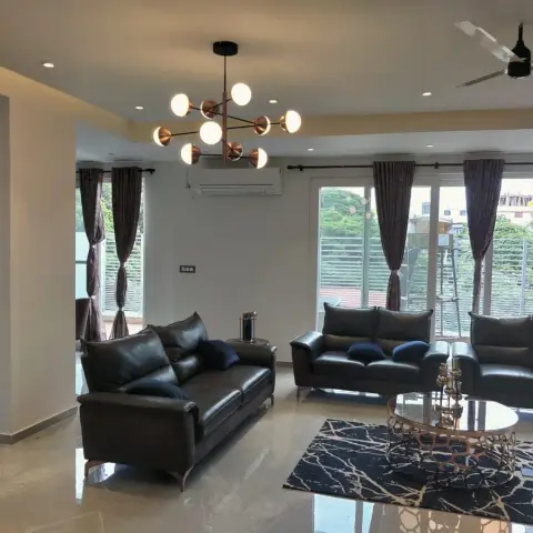 Large daylit living room with three dark leather sofas around an oval mirror-top coffee table on a black-and-gold marbled rug