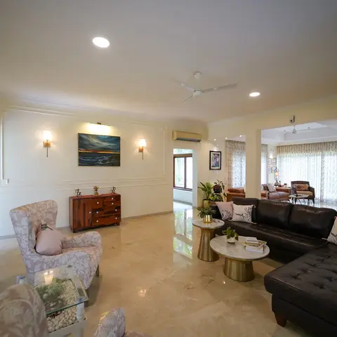 Large living room with a moulded feature wall framing a seascape painting between brass sconces, a dark leather sectional sofa