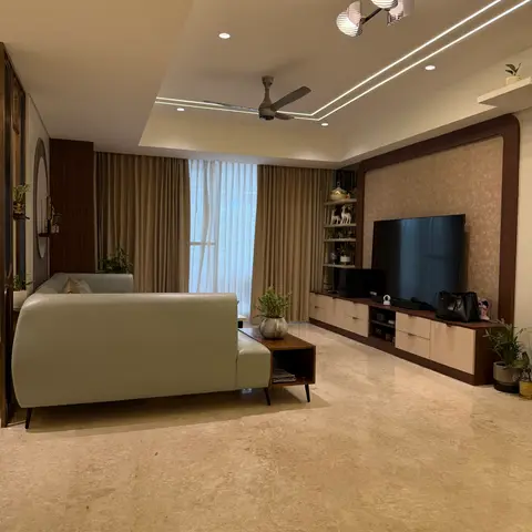 Large living room with a sage-green leather sofa facing a wood-framed textured TV wall, a cove-lit tray ceiling with a sculptural pendant