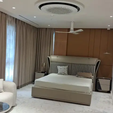 Large master bedroom with a tan leather-panelled headboard wall behind a cream leather bed, a curved boucle sofa on white marble