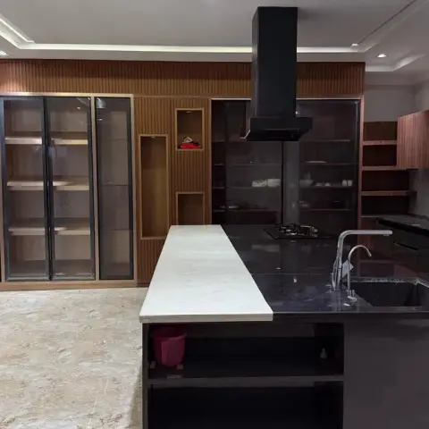 Large open kitchen with a dark stone island topped by a white marble waterfall countertop extension, glass-front display cabinetry