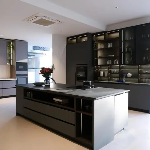 Large open kitchen with a dark stone-topped island, matte grey base cabinets and a backlit open shelving wall displaying glassware and crockery.