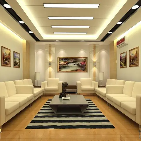 Large symmetrical living hall with two long cream sofas facing each other under a multi-tier cove-lit ceiling, flanked by framed landscape paintings.