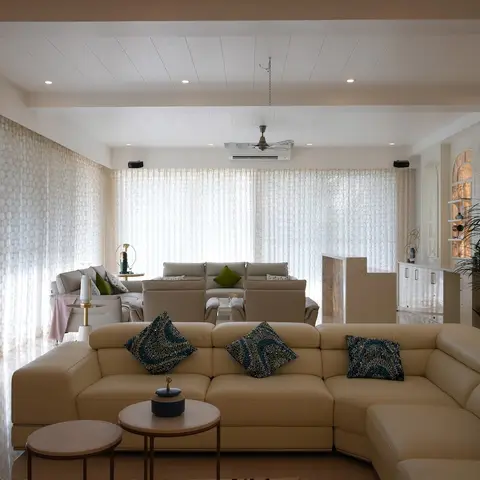 Large villa living room with a cream leather sectional and sequinned teal accent cushions in front of floor-to-ceiling sheer curtains along a full glass wall.