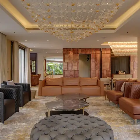 Large villa living room with tan leather sofas and quilted charcoal armchairs around a grey buttoned ottoman and stacked stone tables
