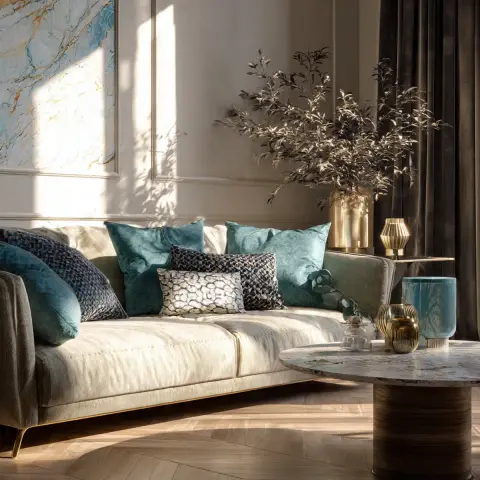 Late-afternoon light rakes across a cream sofa on a slim brass plinth, teal and printed velvet cushions