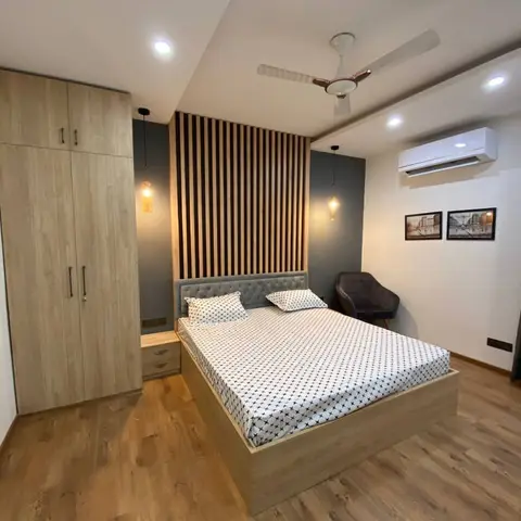 Light-oak platform storage bed with a grey tufted headboard under a floor-to-ceiling oak batten panel on charcoal