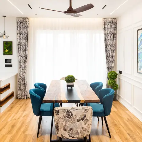 Live-edge acacia dining table with a black resin river running down its centre, four teal velvet barrel chairs and one monstera-print armchair at the head
