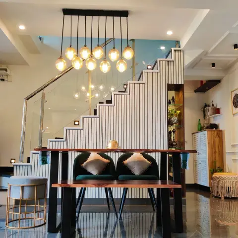 Live-edge wood dining table with black metal legs and green velvet chairs, a cluster of amber glass globe pendants, set before a fluted-panel staircase
