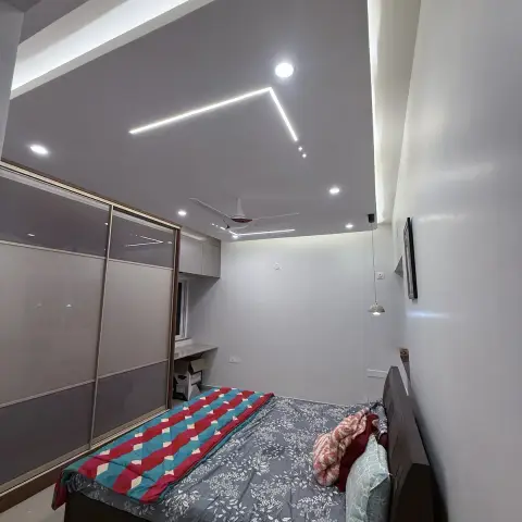 Lived-in bedroom shot from the doorway: a dark wood double bed under mismatched quilts, a full-height sliding wardrobe in grey lacquered glass